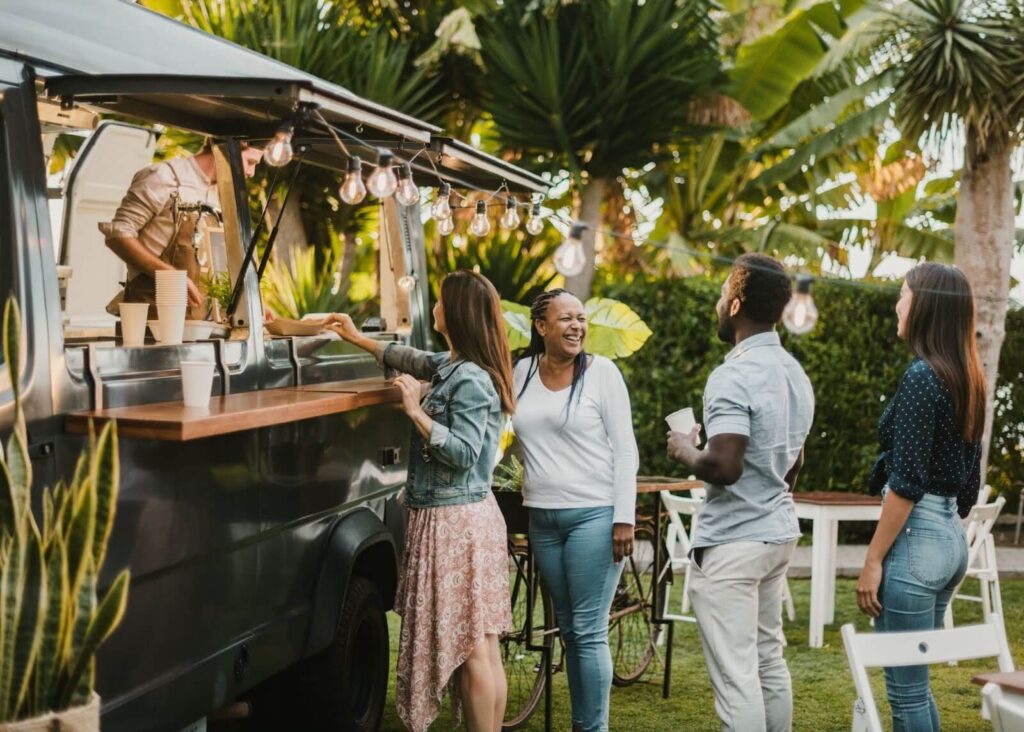 Guests happily ordering from a food truck at an outdoor event surrounded by lush greenery.